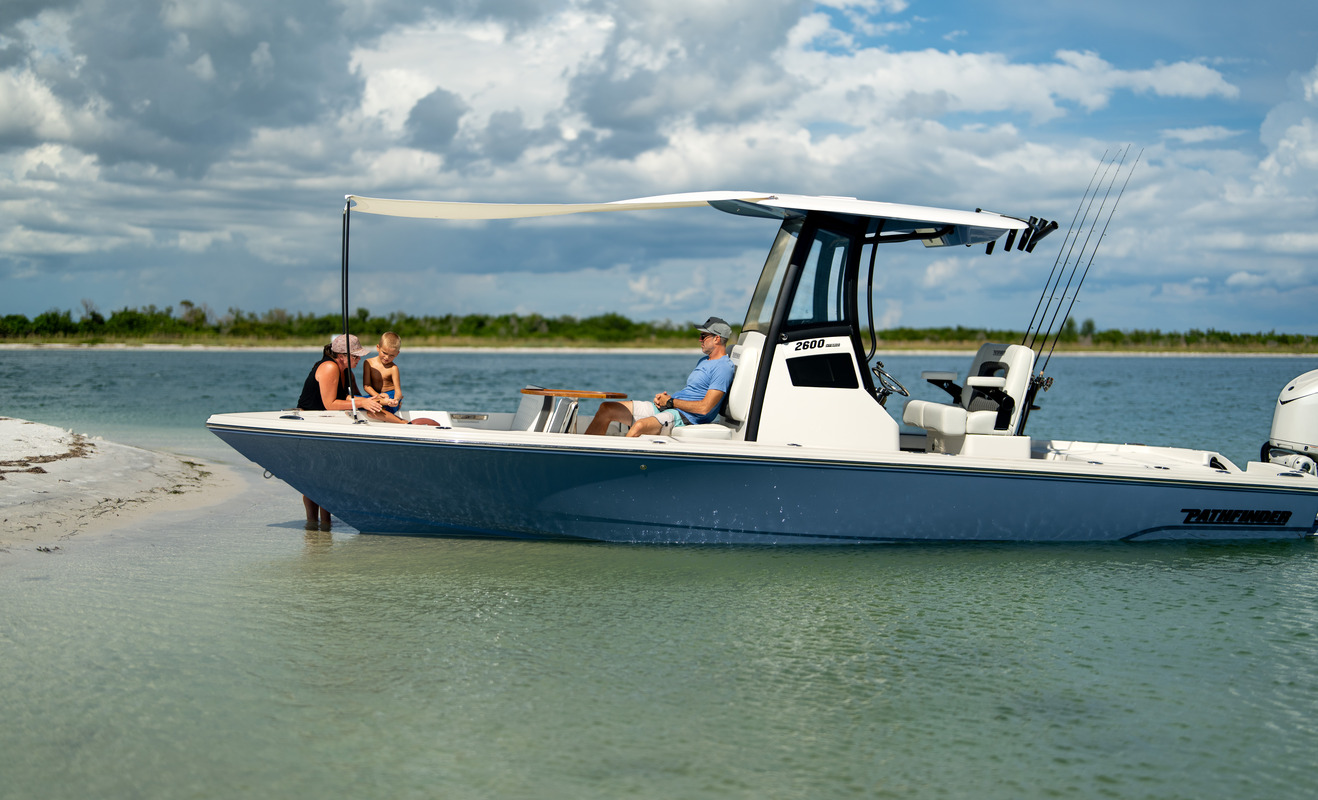 Pathfinder 2600 Hybrid beached on a sandbar with its bow shade canopy extended, a family of three aboard relaxing under the shade.